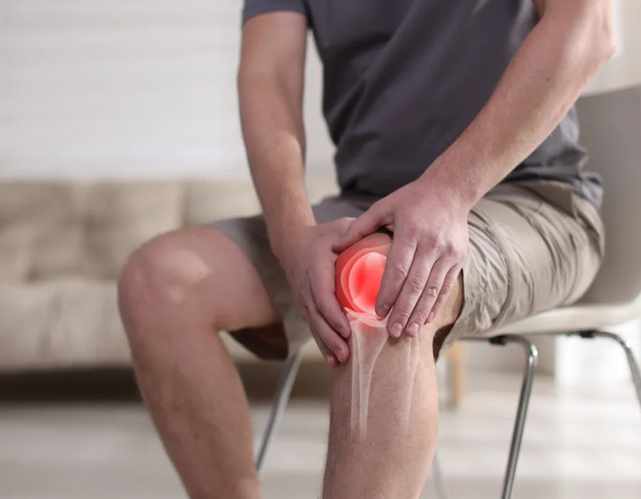 Seated man holding his knee with the joint highlighted in red, illustrating chronic joint pain